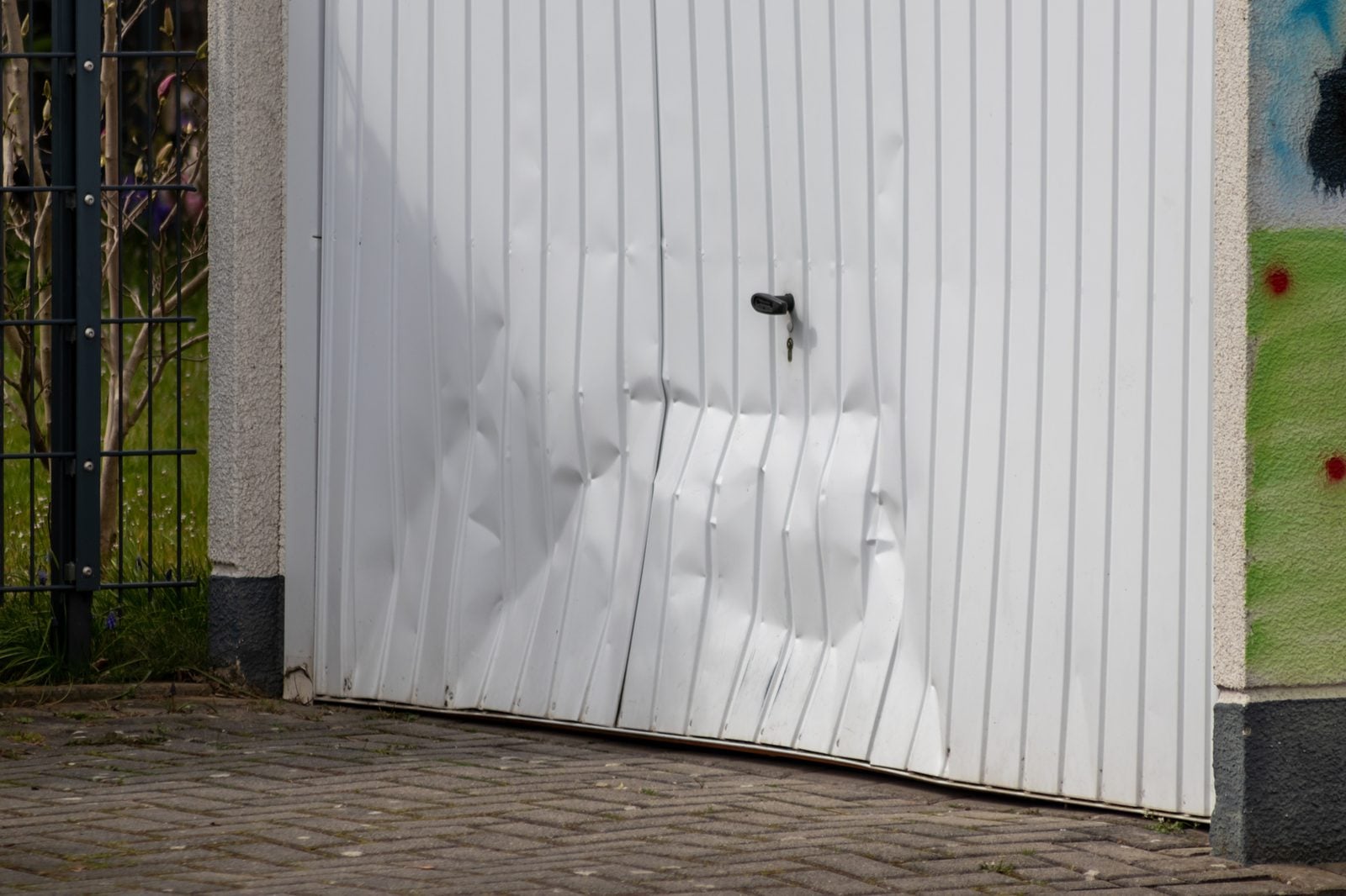 Dented and damaged white garage door panel after impact
